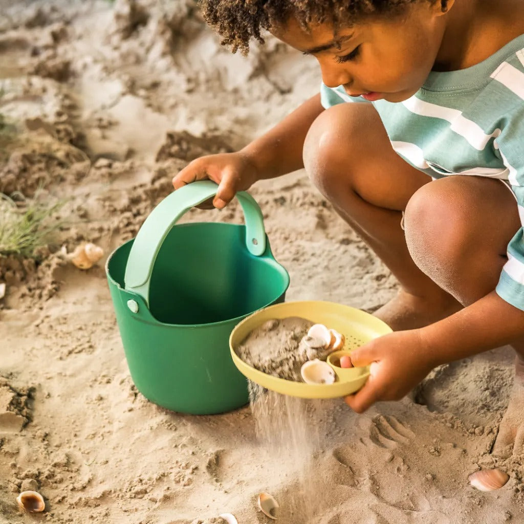 Kid using beach bucket and sifter toy in sand play